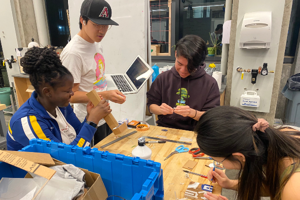 Four students sitting at table working with various materials