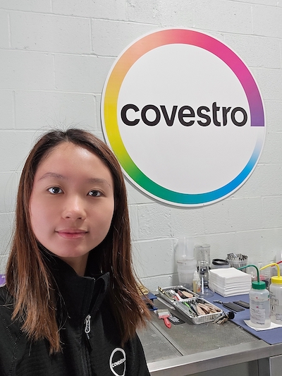 Phylicia Ma stands in front of workstation with Covestro sign in background