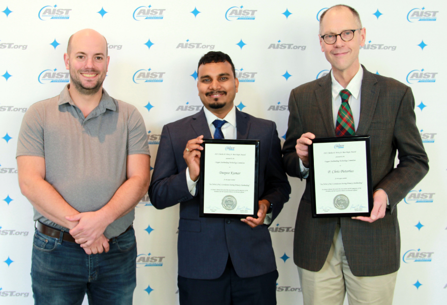 three men standing with two holding awards