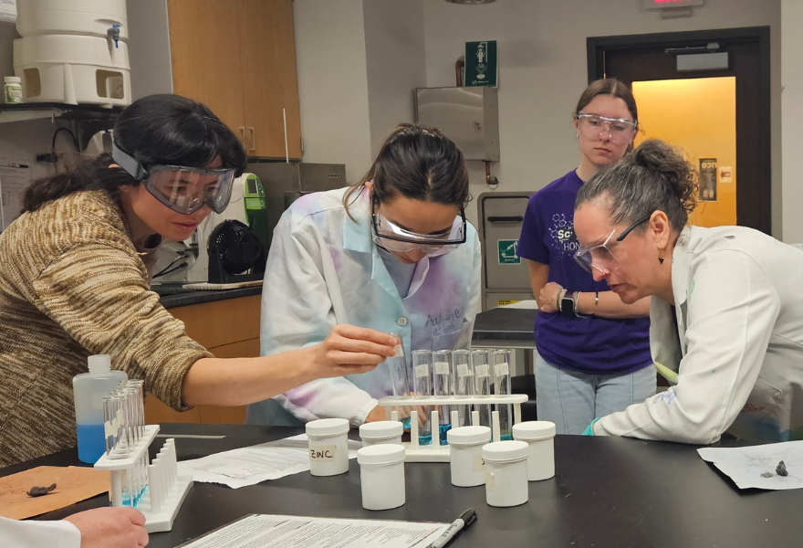 A group of four women in a science lab conduct an experiment with test tubes