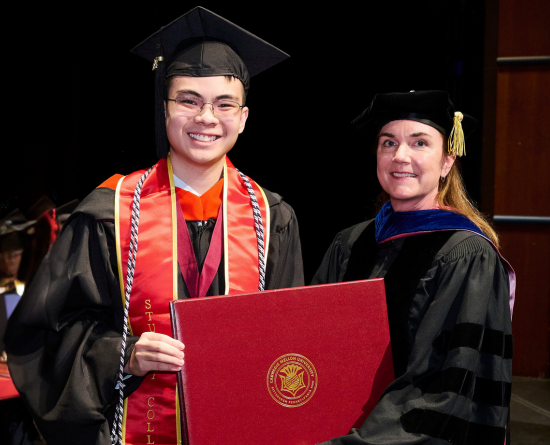 Adrian Tran holding diploma case standing next to Beth Dickey