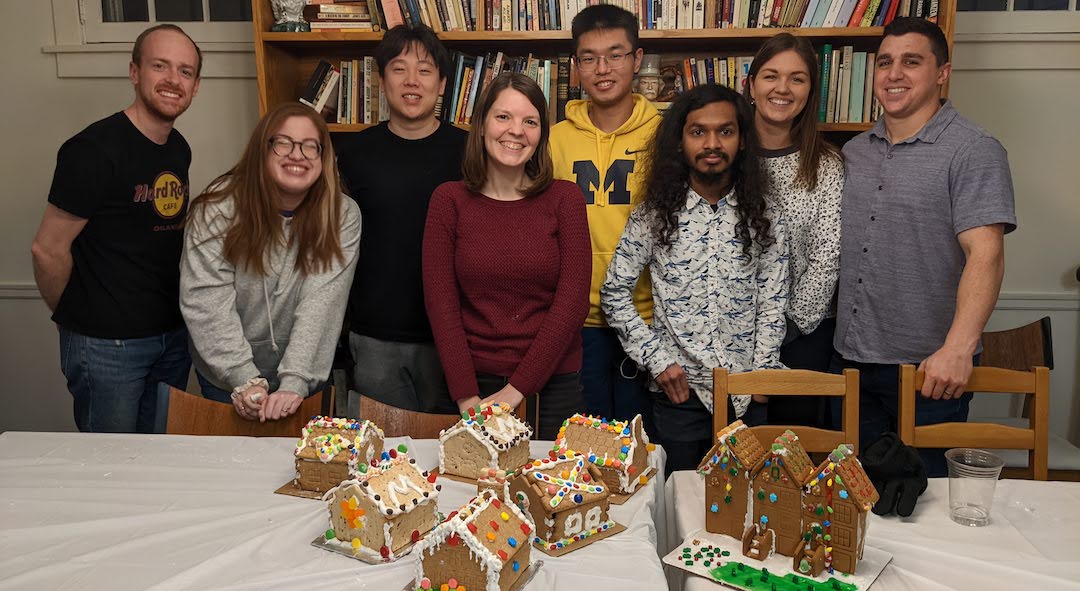 Krause Group members pose with decorated gingerbread houses at holiday gathering